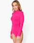 A woman modeling a bright pink long-sleeve bodysuit with a mock neck, photographed against a clean white studio background.