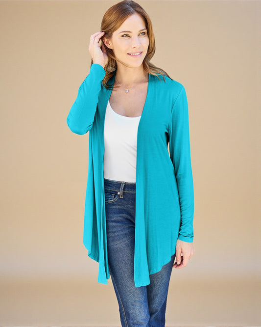 Woman wearing a turquoise cardigan over a white top and blue jeans on a beige background