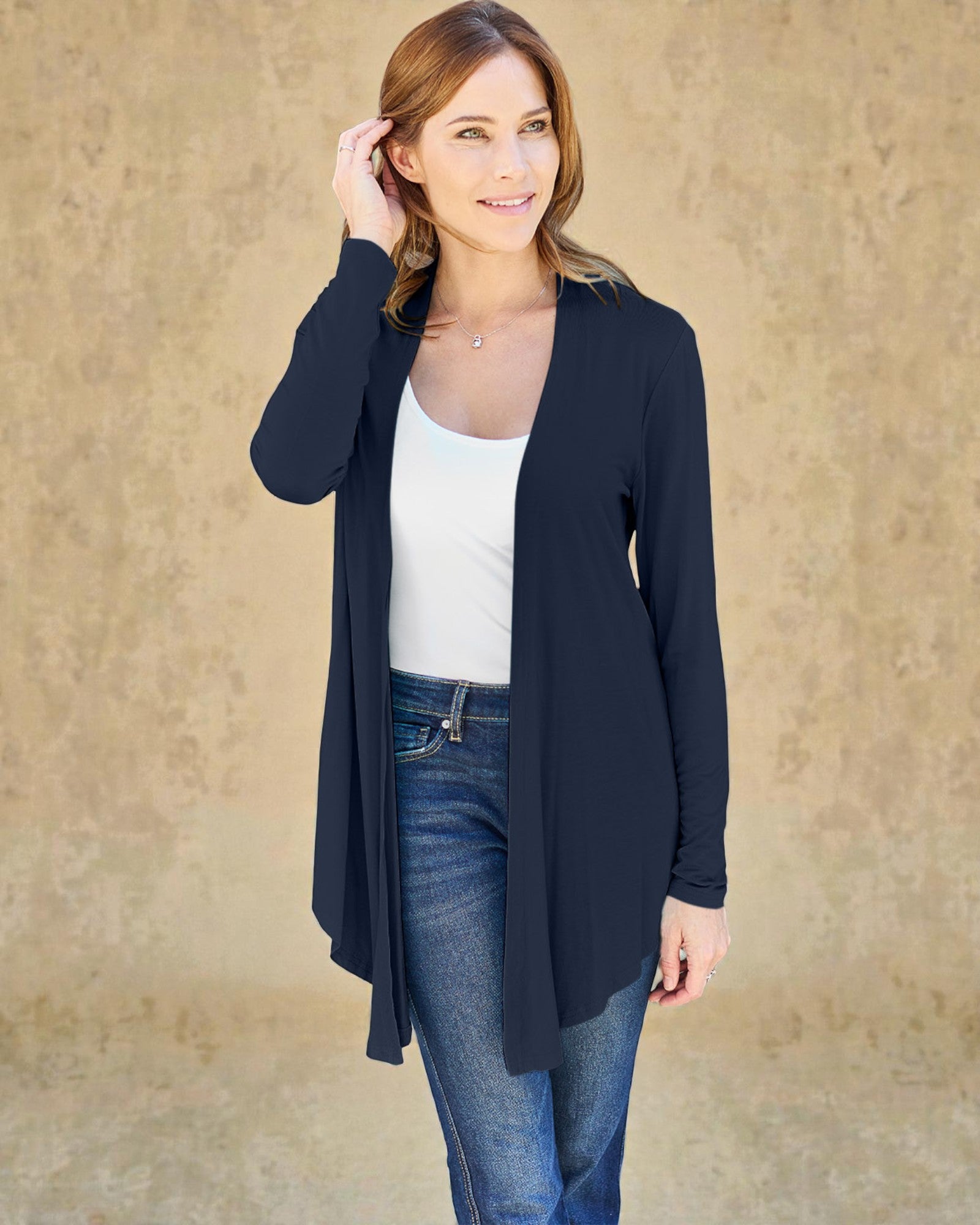 Woman wearing a navy cardigan over a white top and blue jeans against a beige background