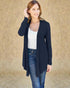 Woman wearing a navy cardigan over a white top and blue jeans against a beige background