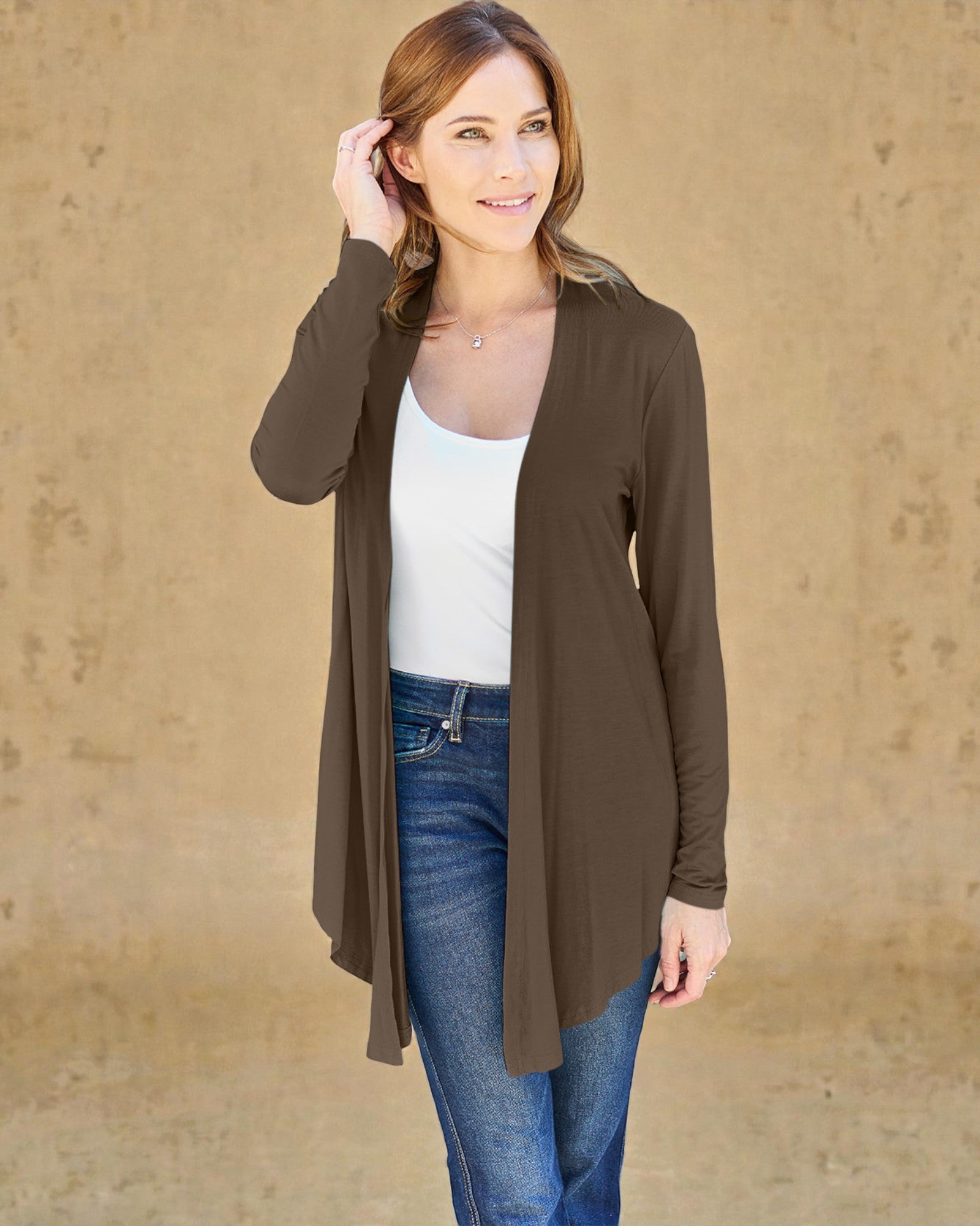 Woman wearing a brown cardigan over a white top and blue jeans against a beige background