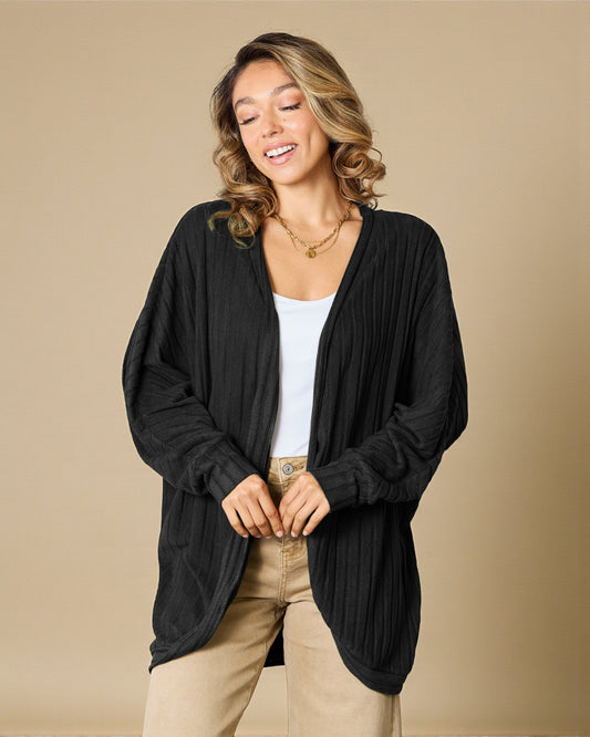 Woman wearing a black cardigan over a white shirt and beige pants on a beige background