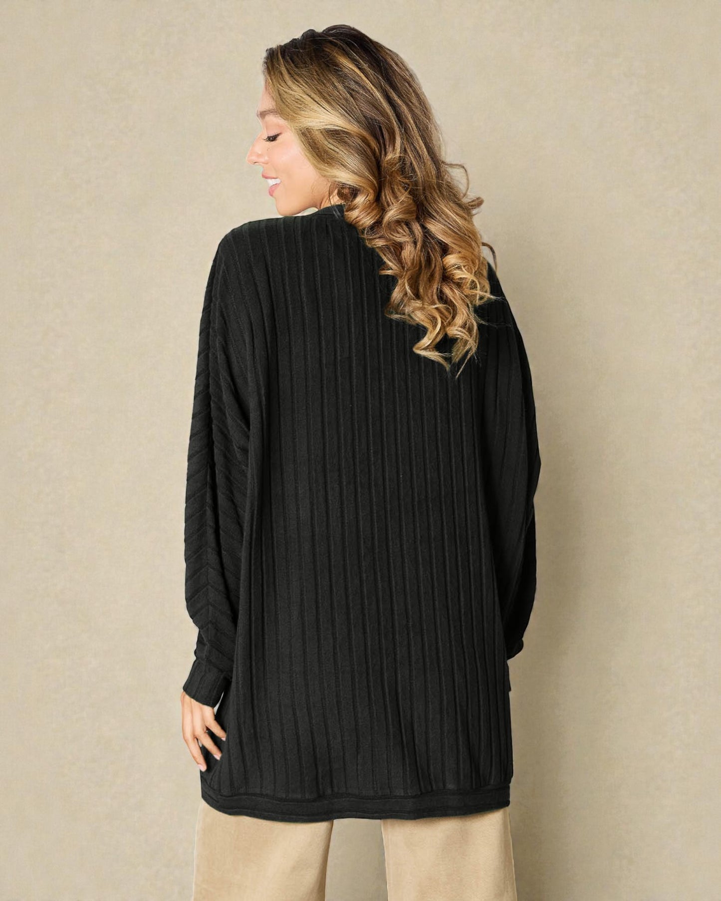 Woman wearing a black ribbed sweater against a beige background