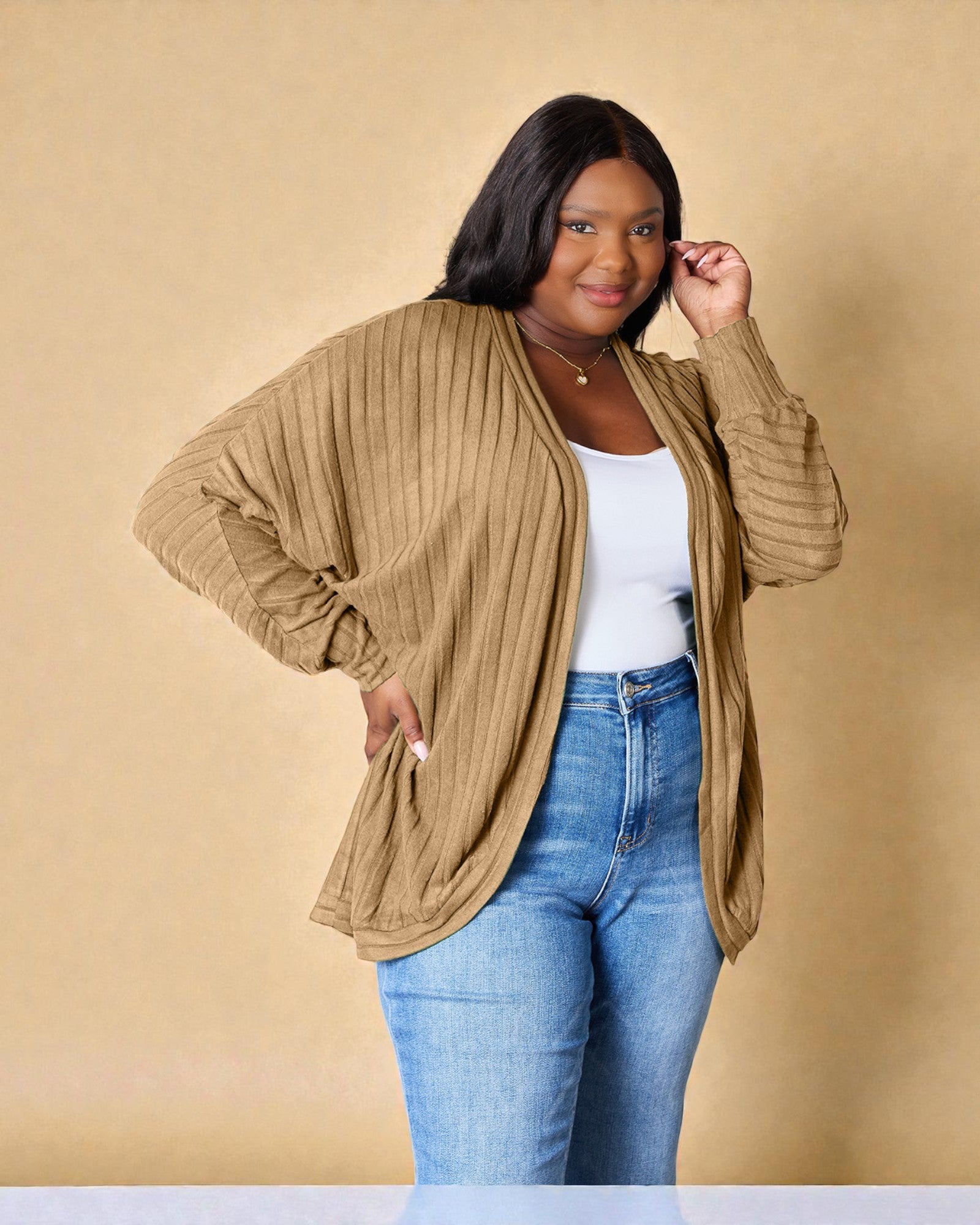 Woman wearing a beige cardigan, white top, and blue jeans against a beige background