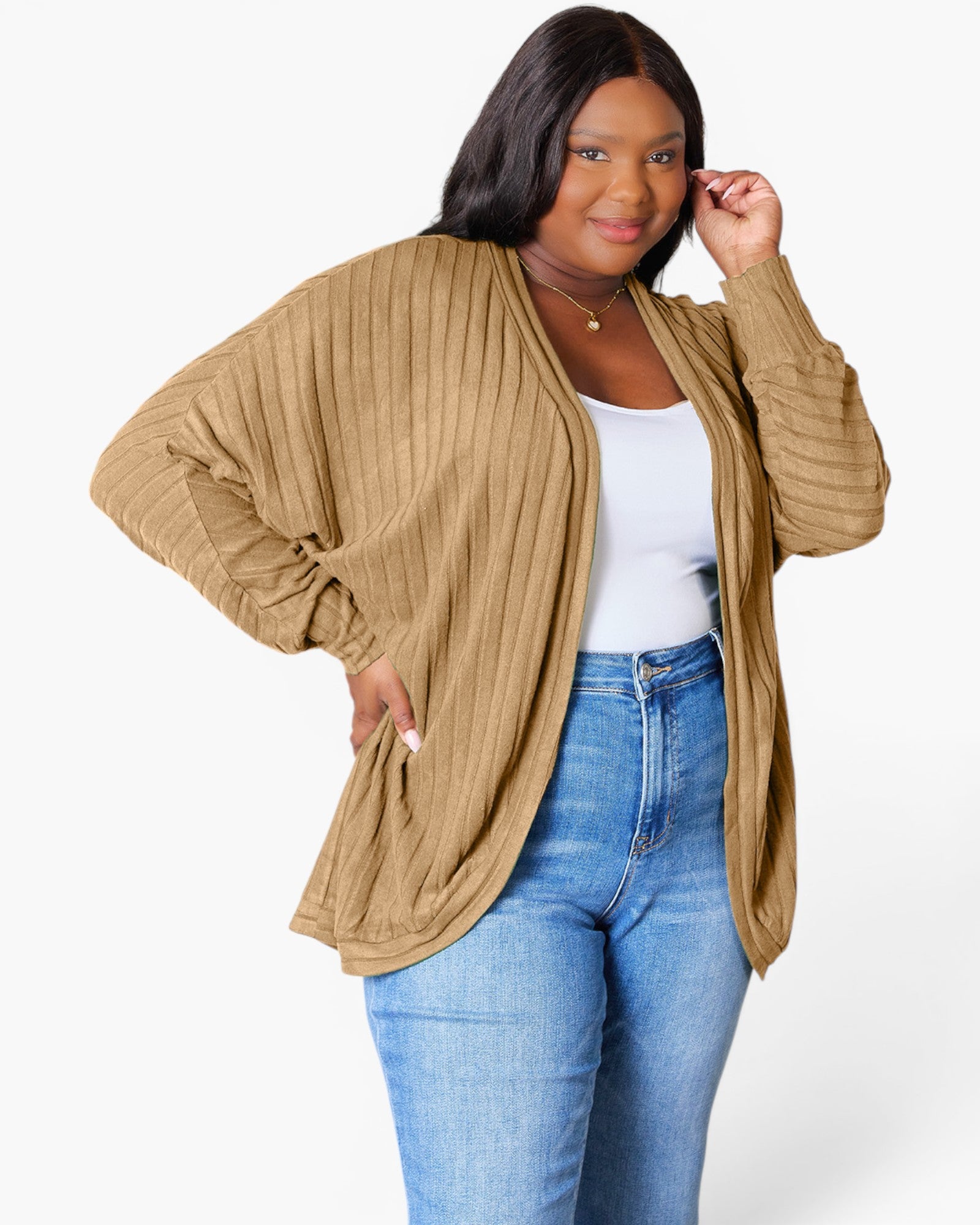 A woman modeling a tan ribbed open-front cardigan with wide draped sleeves, worn over a white tank top and blue jeans against a light gray studio background.