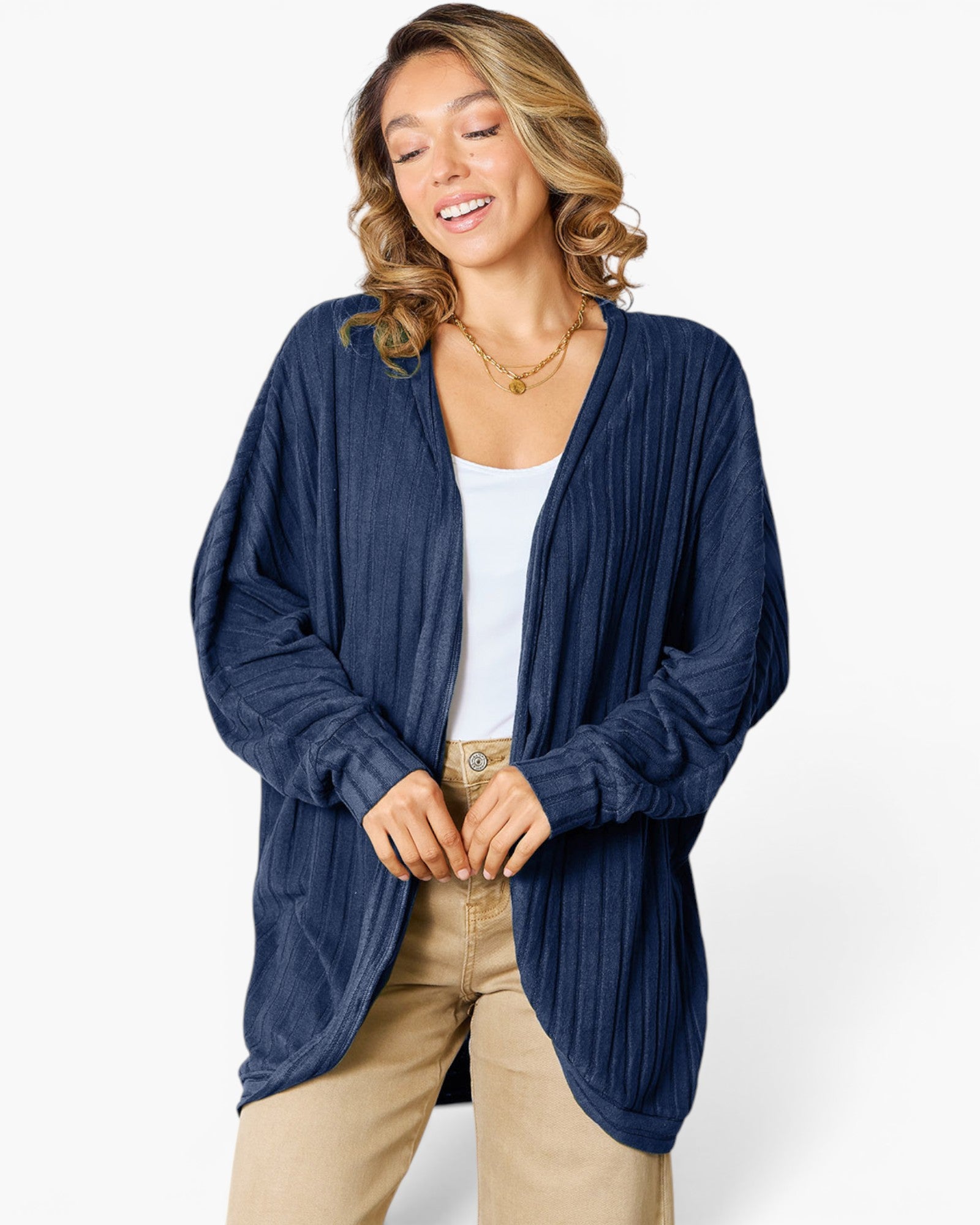 A woman wearing a navy blue open-front cardigan with a textured, vertically pleated fabric over a white tank top and beige pants, photographed against a clean white studio background.