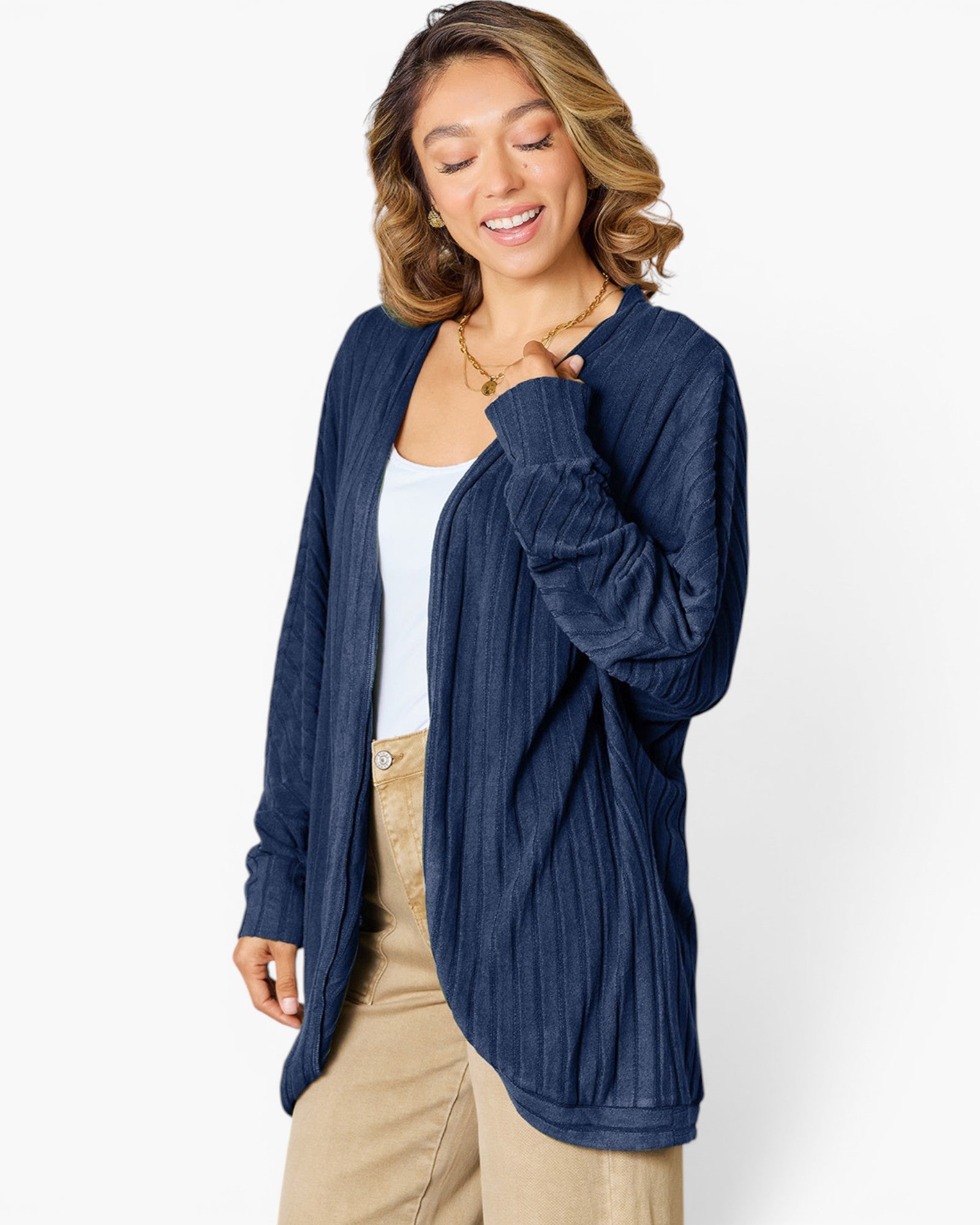 A woman wearing a navy blue textured open-front cardigan over a white tank top and beige pants, photographed against a clean white studio background.