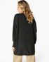A woman shown from the back wearing a black ribbed knit long-sleeve sweater and beige pants against a plain white studio background.