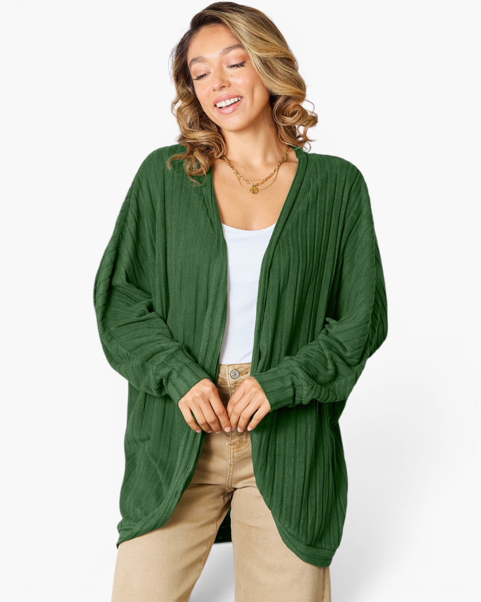 A woman wearing a dark green, long-sleeve, open-front cardigan with a textured crinkle fabric, styled over a white top and beige pants, against a plain white studio background.