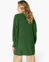 A woman shown from the back wearing an oversized green ribbed knit sweater, paired with beige pants, against a plain white studio background.