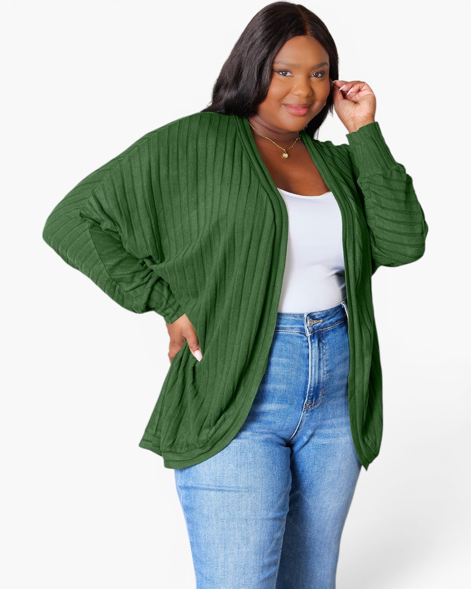 A woman modeling a green ribbed open-front cardigan with balloon sleeves, worn over a white tank top and blue jeans, against a plain white studio background.