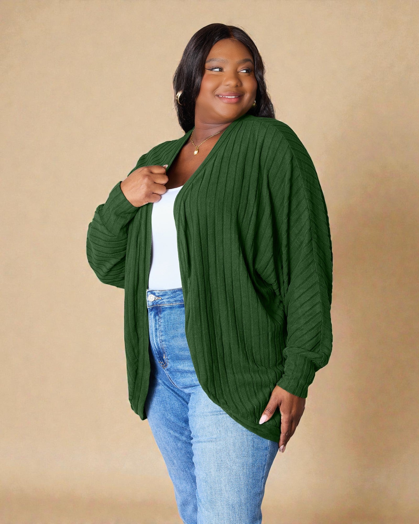 Woman wearing a green cardigan over a white top and blue jeans on a beige background