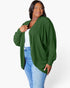 A woman modeling a dark green ribbed knit cardigan with long sleeves, worn open over a white top and blue jeans, against a plain white studio background.