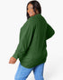 A woman wearing a dark green ribbed knit sweater and blue jeans, photographed from the back against a plain light gray studio background.