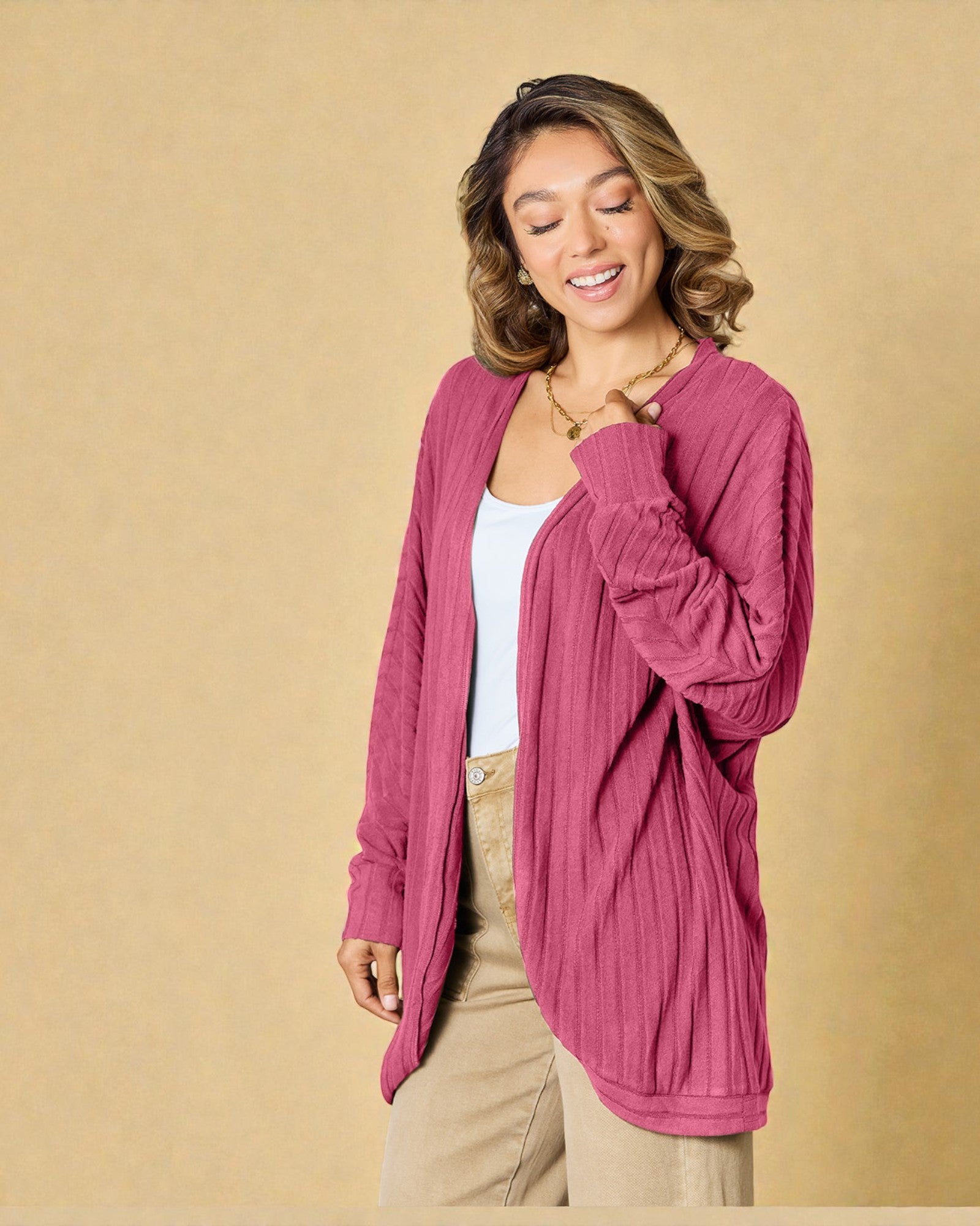 Woman wearing a pink cardigan over a white top and beige pants on a beige background