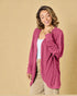 Woman wearing a pink cardigan over a white top and beige pants on a beige background