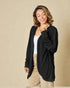 Woman wearing a black cardigan over a white top and beige pants on a beige background