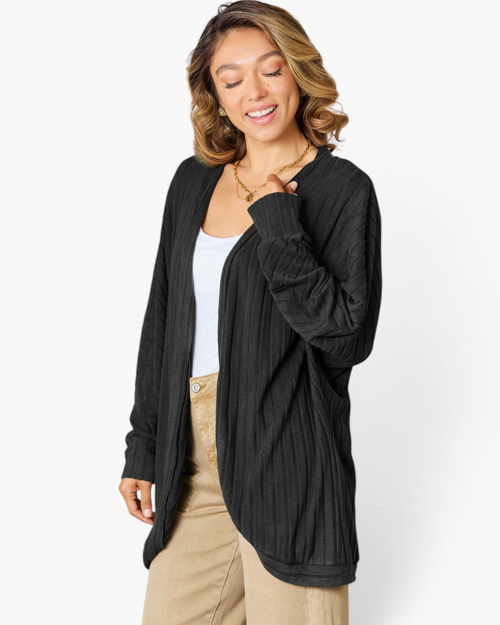 A woman wearing a black long-sleeve open-front cardigan with a textured vertical pleated pattern, styled over a white tank top and beige pants, against a plain white studio background.