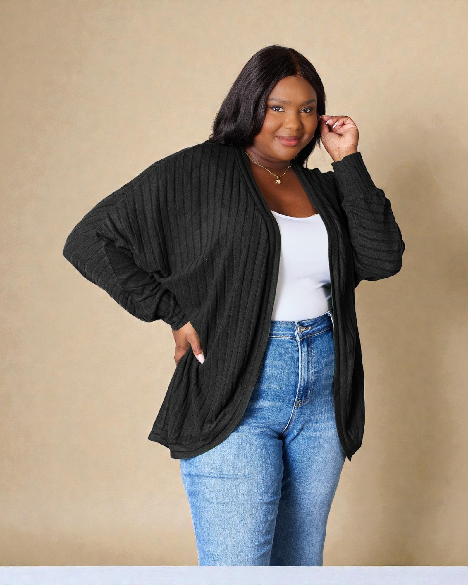 Woman wearing a black cardigan over a white top and blue jeans on a beige background