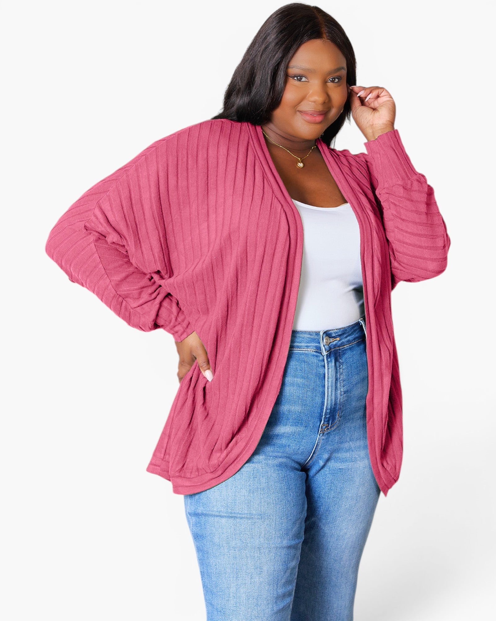 A woman modeling a pink ribbed open-front cardigan with voluminous balloon sleeves, worn over a white tank top and blue jeans against a plain white studio background.