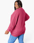A woman wearing a bright pink ribbed knit sweater with blue jeans, photographed against a clean white studio background.