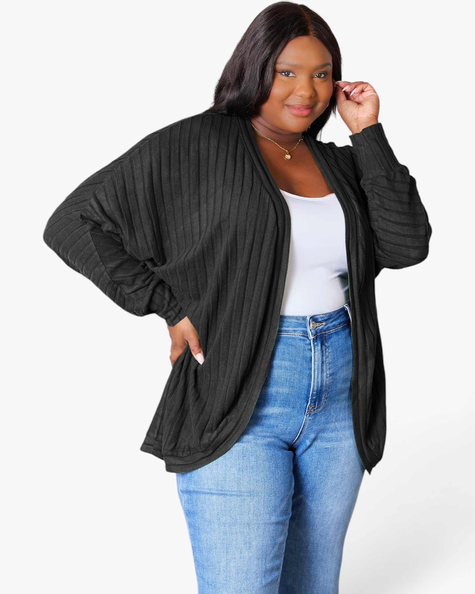 A woman modeling a black ribbed open-front cardigan with balloon sleeves, worn over a white tank top and blue jeans, against a light gray studio background.