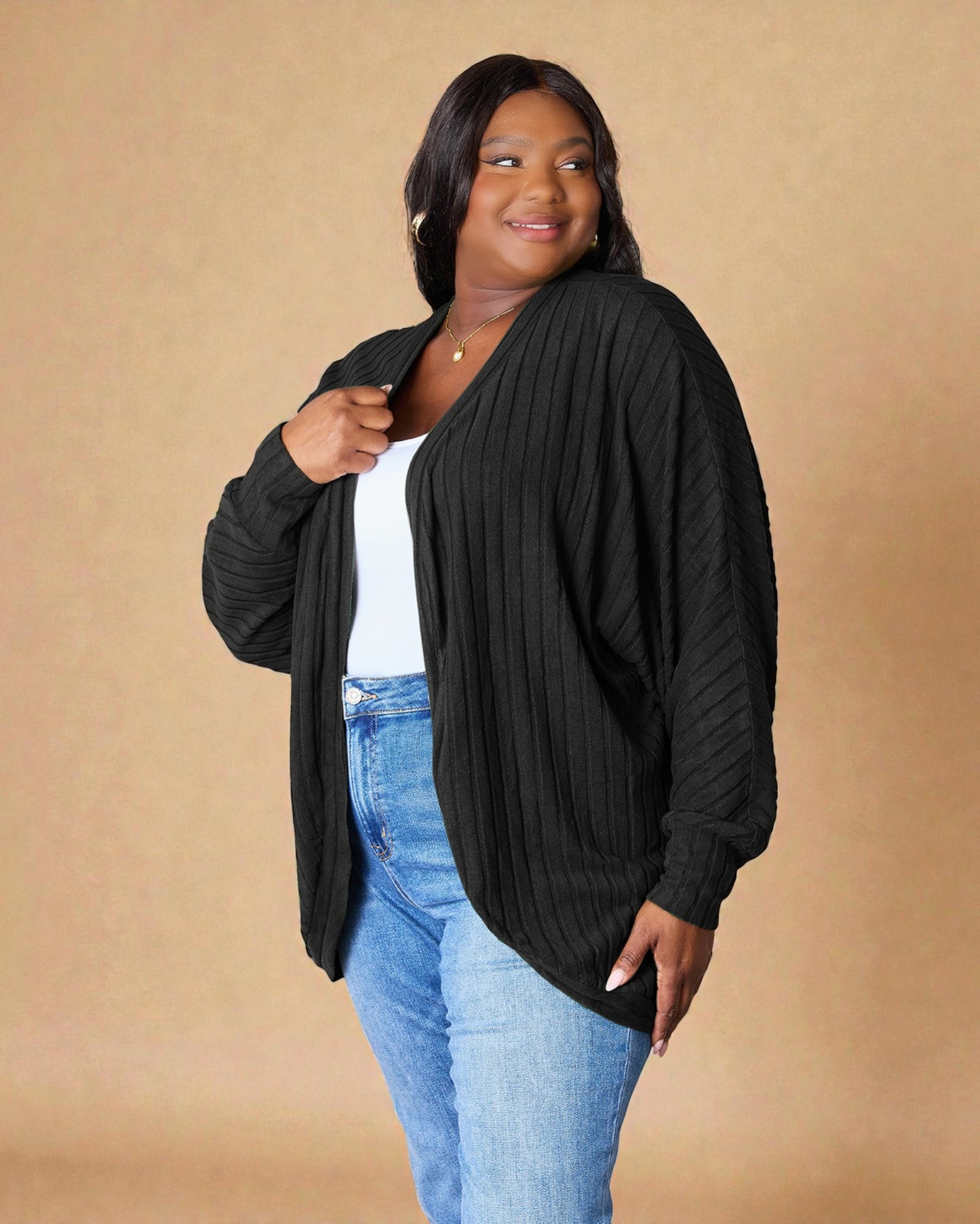 Woman wearing a black cardigan over a white top and blue jeans on a beige background