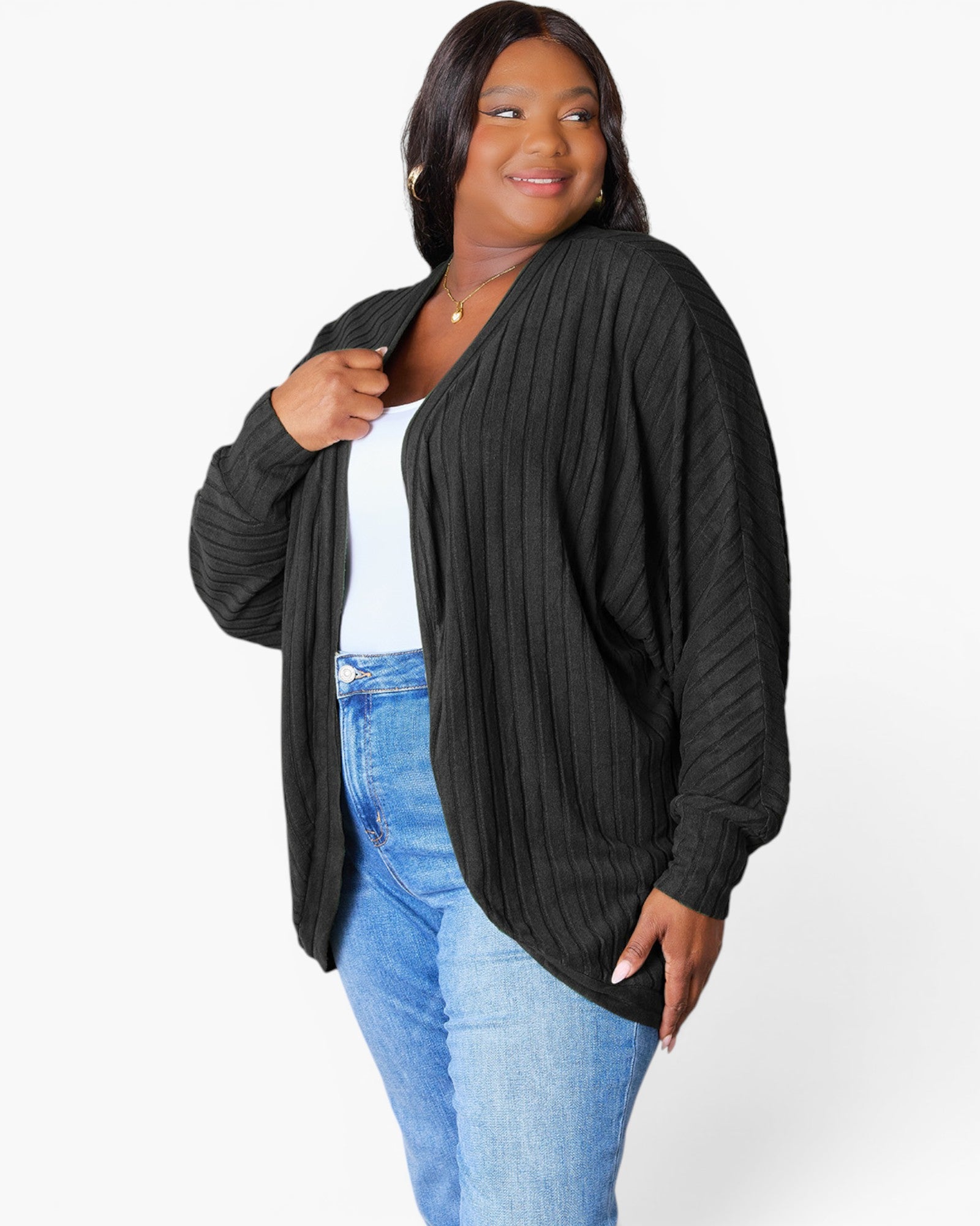 A woman modeling a black ribbed open-front cardigan with long sleeves, worn over a white top and blue jeans, against a plain white studio background.