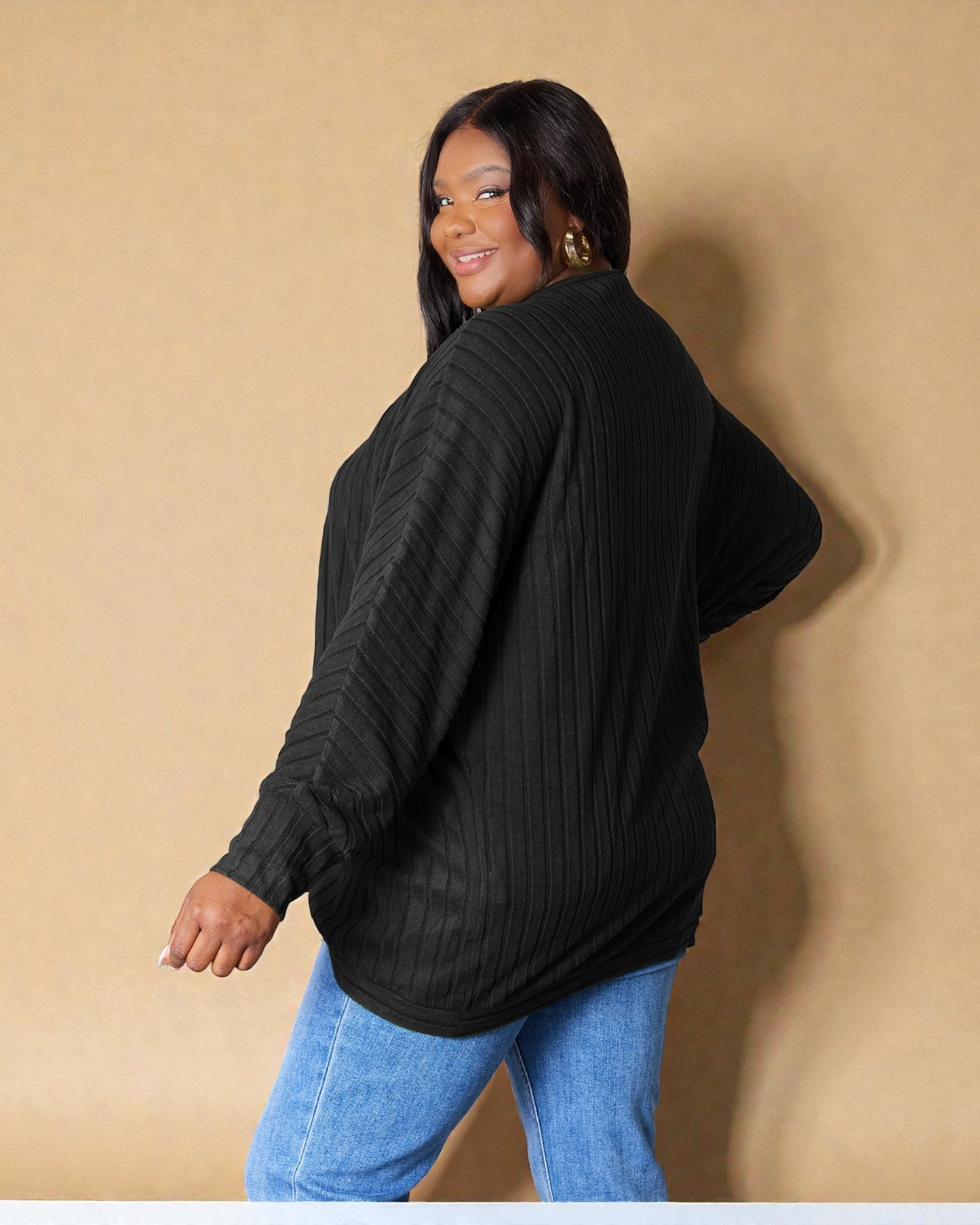 Woman wearing a black sweater and blue jeans against a beige background