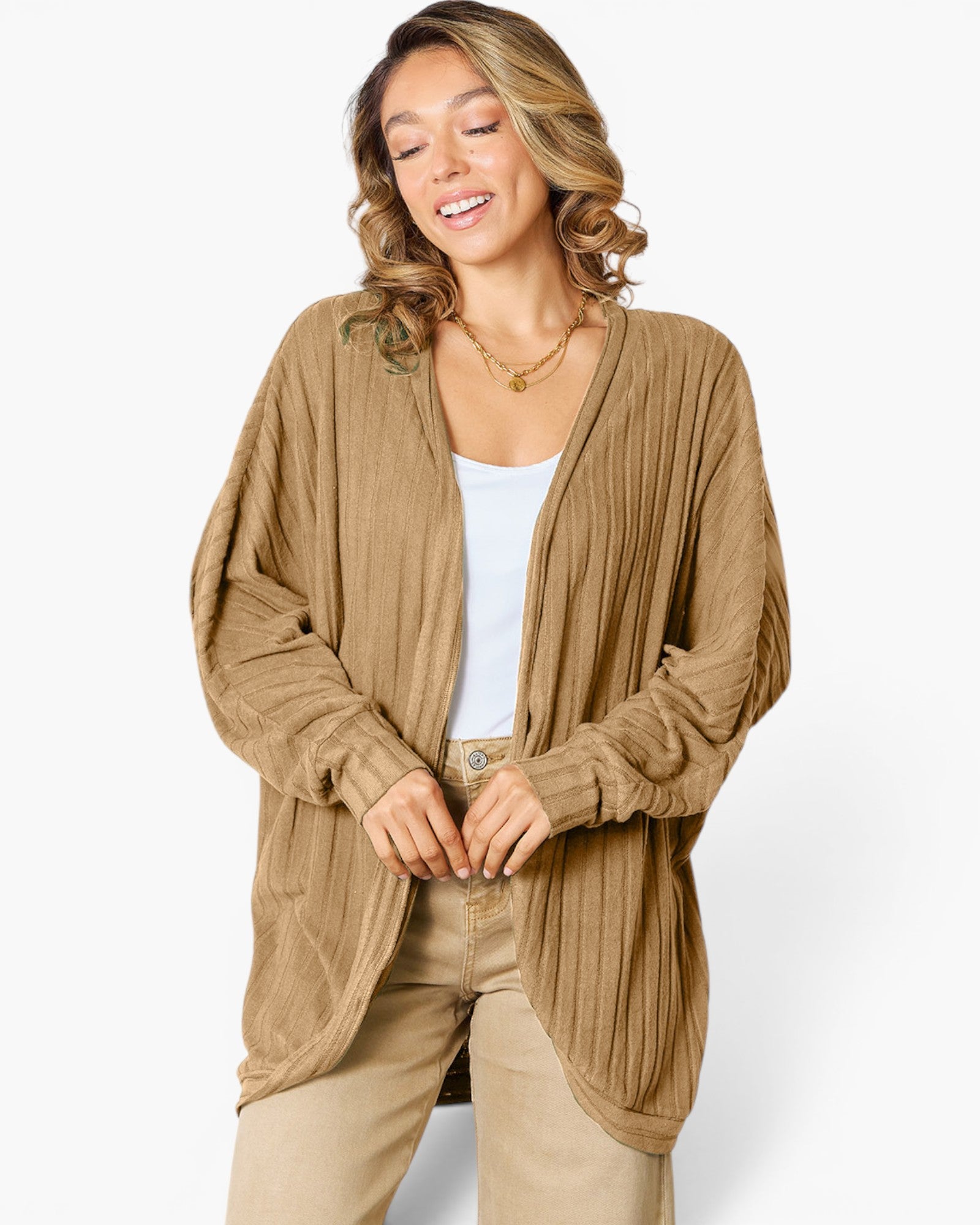 A woman wearing a tan open-front cardigan with a textured, pleated or ribbed knit pattern, layered over a white tank top and beige pants, photographed against a clean white studio background.