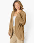 A woman wearing a tan ribbed knit cardigan over a white tank top and beige pants, photographed against a clean white studio background.