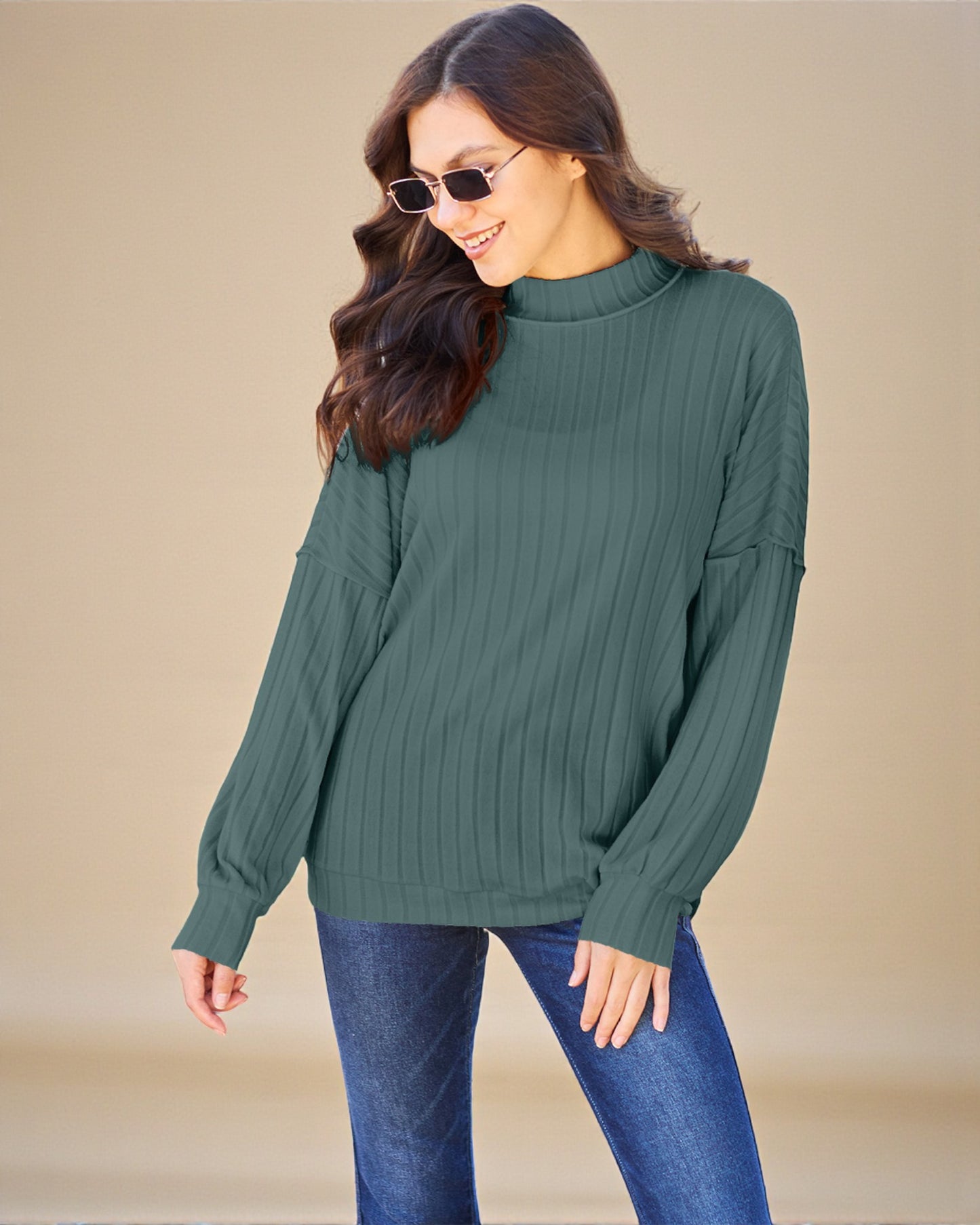 Woman wearing a green ribbed sweater and blue jeans against a beige background