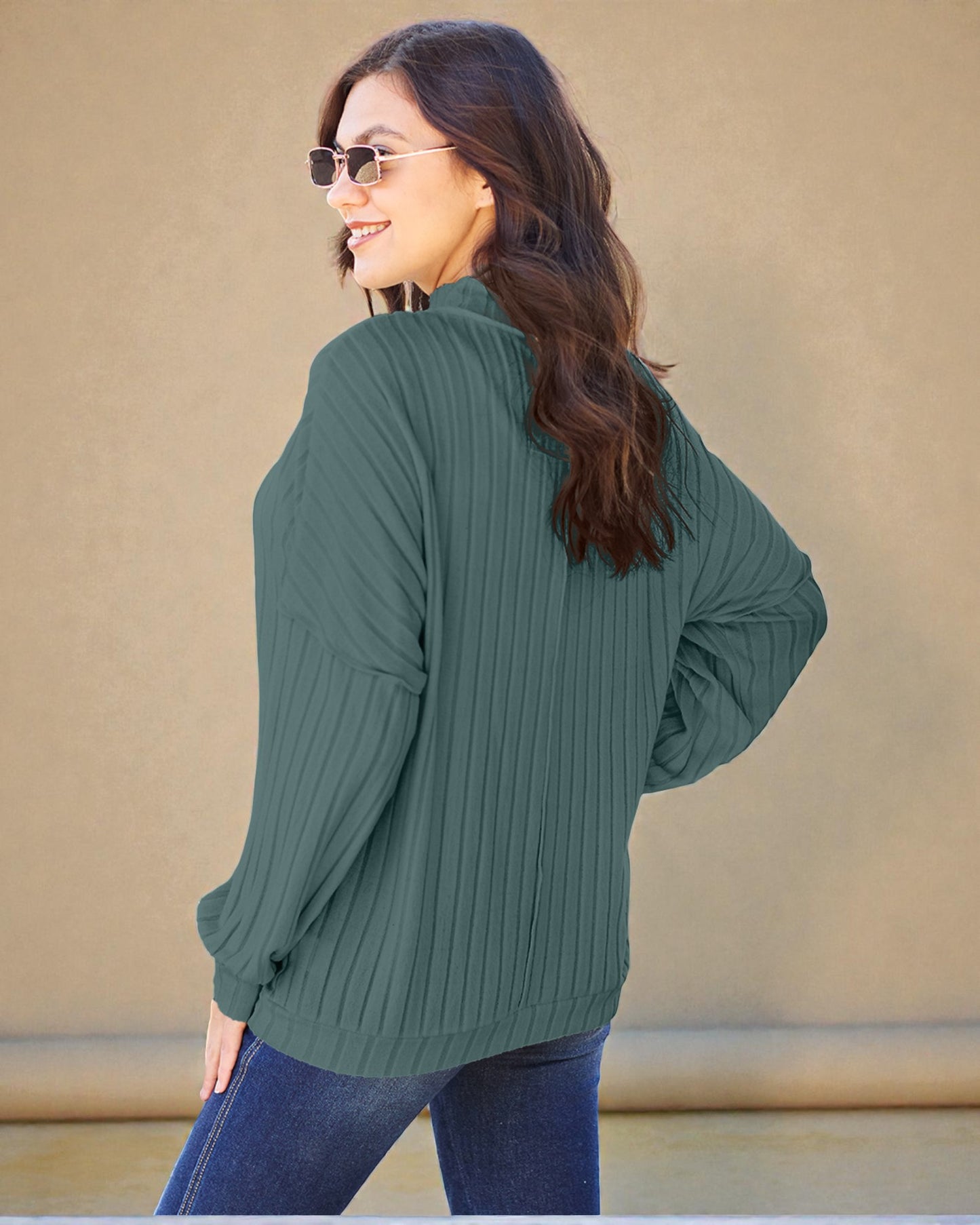 Woman wearing a green ribbed sweater and sunglasses against a beige background