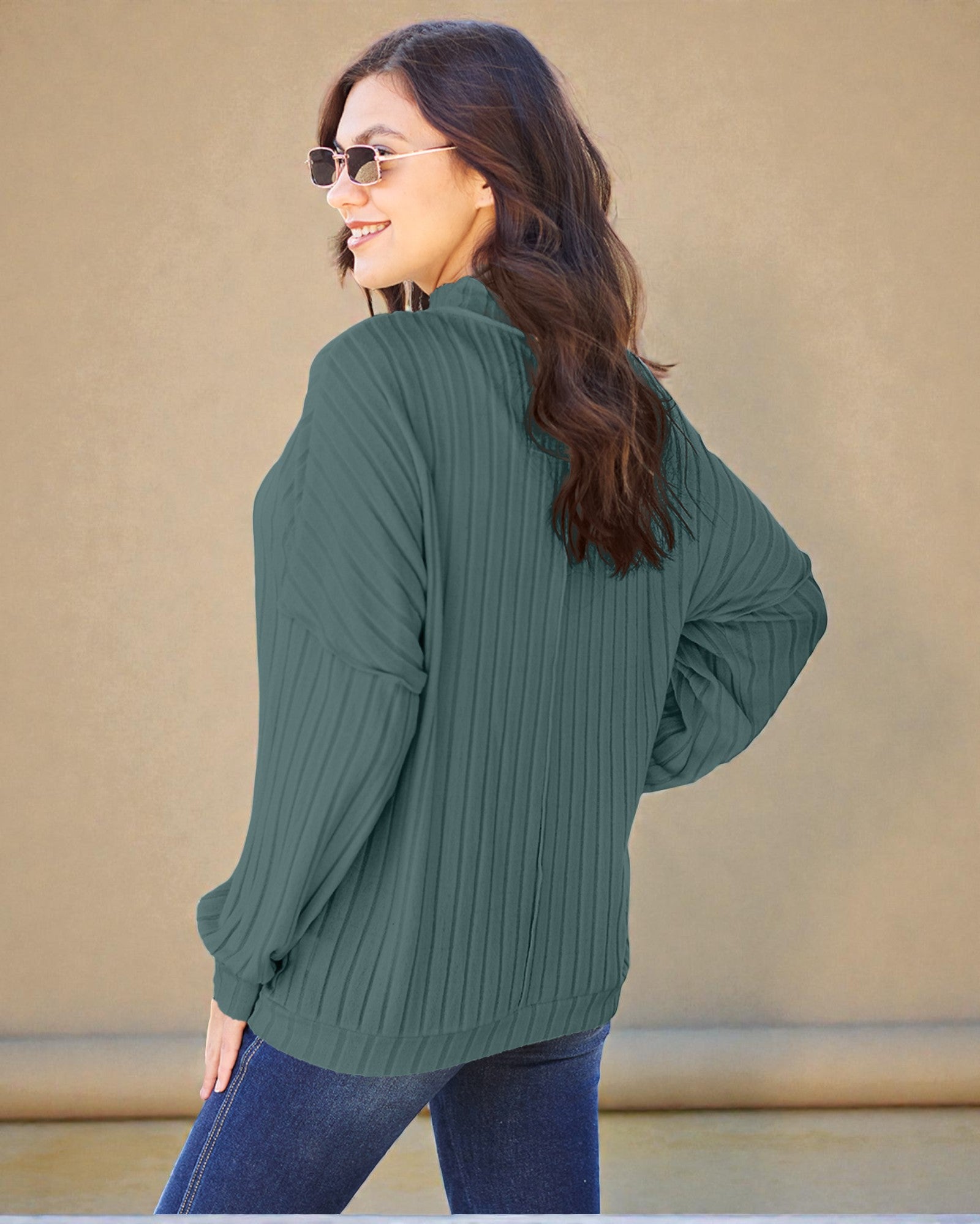 Woman wearing a green ribbed sweater and sunglasses against a beige background