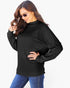 A woman wearing a black ribbed long-sleeve mock neck sweater and blue jeans, posing against a plain white background.