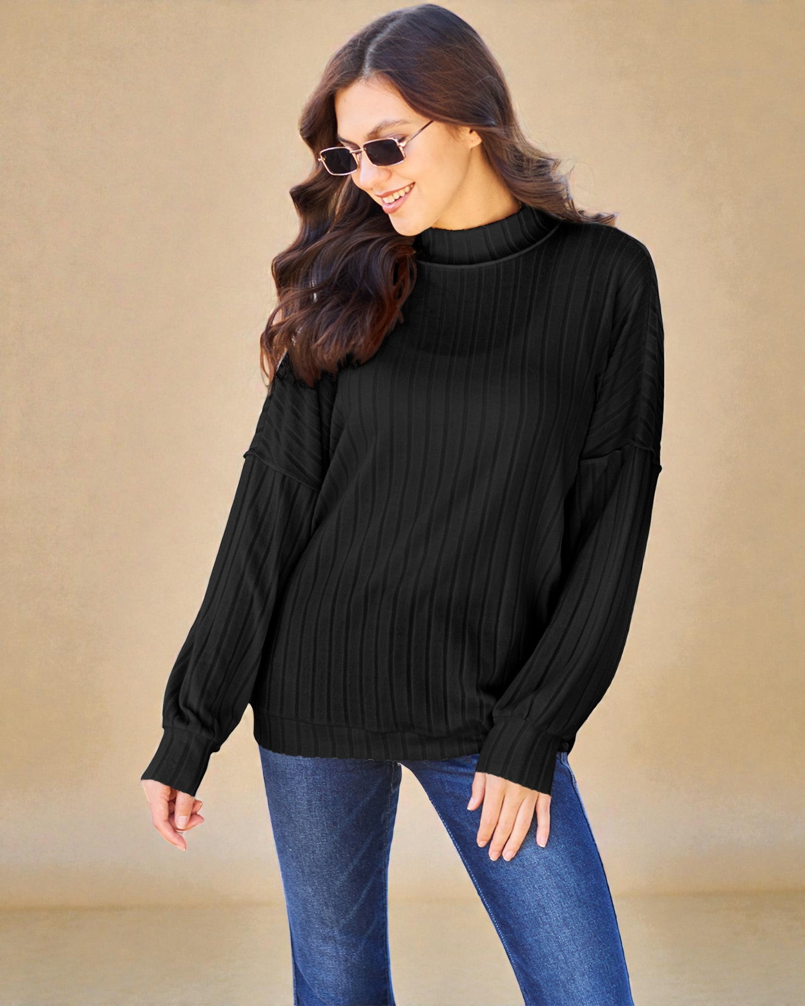 Woman wearing a black ribbed sweater and blue jeans against a beige background