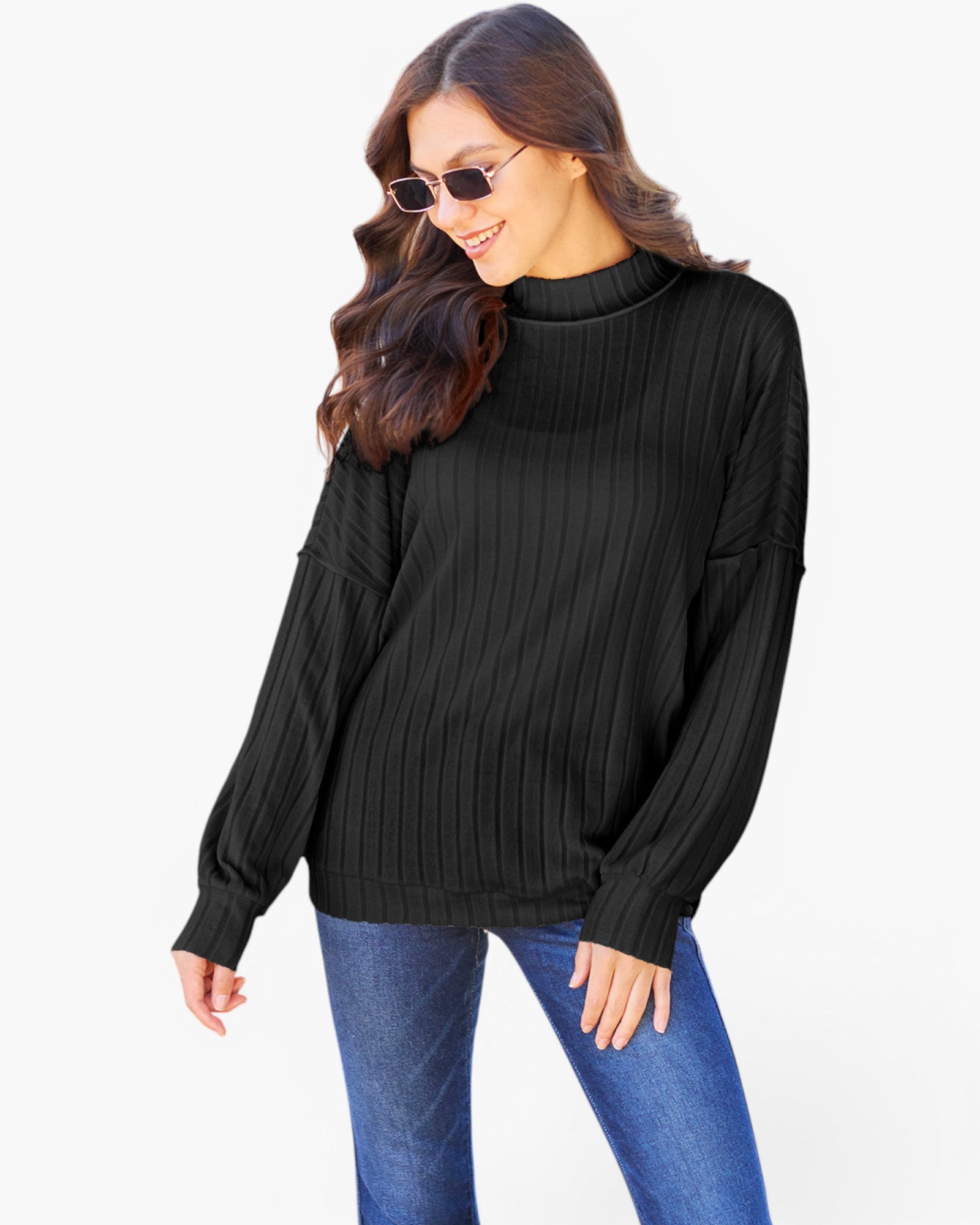 A woman wearing a black ribbed mock neck sweater and blue jeans, posing against a solid white background.