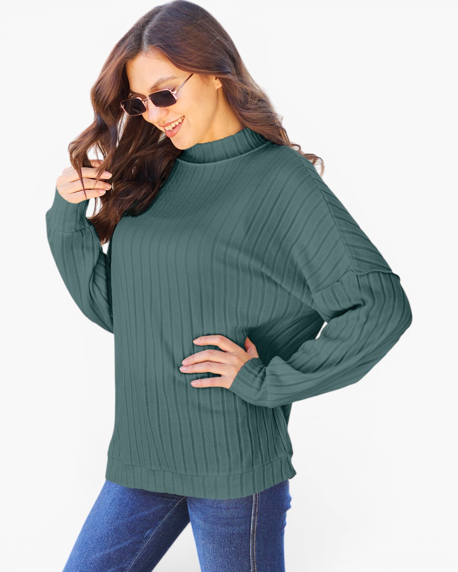 A woman wearing a dark green ribbed knit mock neck sweater and blue jeans, posing against a plain white background.