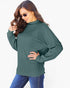 A woman wearing a dark green ribbed knit mock neck sweater and blue jeans, posing against a plain white background.