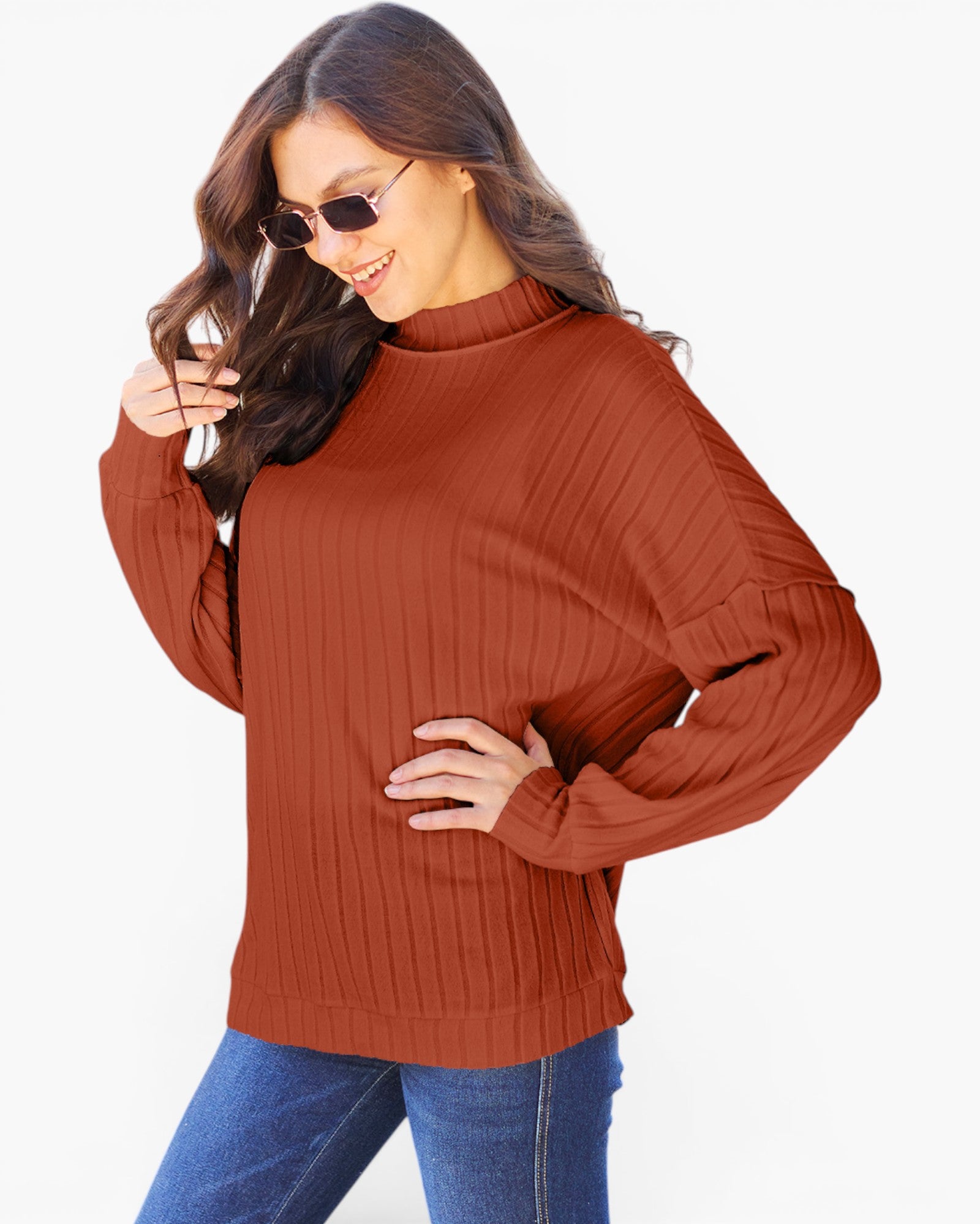 A woman wearing a rust-orange ribbed knit mock-neck sweater with long sleeves and side cutouts, paired with blue jeans, against a plain white background.