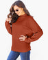 A woman wearing a rust-orange ribbed knit mock-neck sweater with long sleeves and side cutouts, paired with blue jeans, against a plain white background.