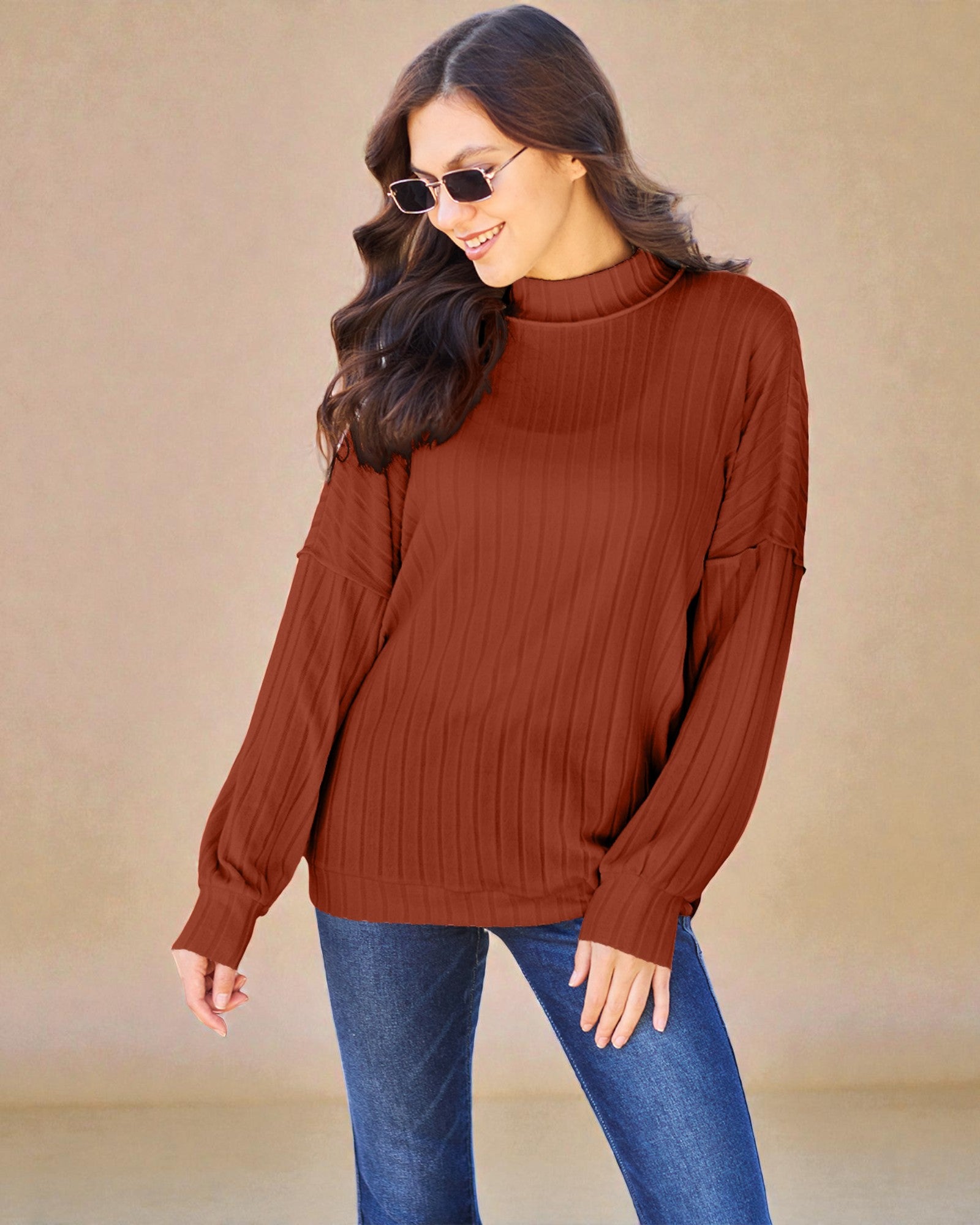 Woman wearing a brown ribbed sweater and blue jeans against a beige background