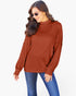 A woman wearing a rust-orange ribbed mock-neck sweater and blue jeans, photographed against a clean white studio background.