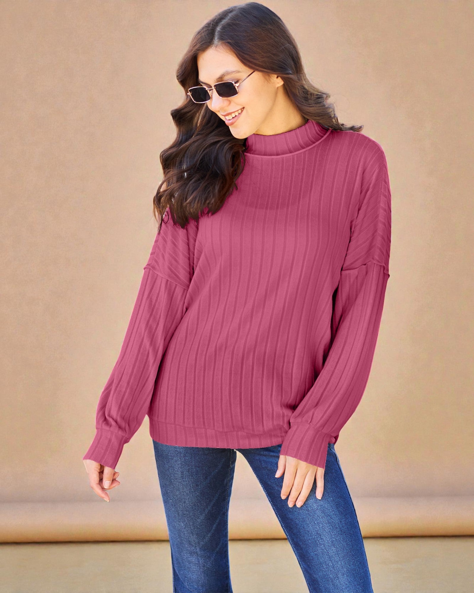 Woman wearing a pink ribbed sweater and blue jeans against a beige background