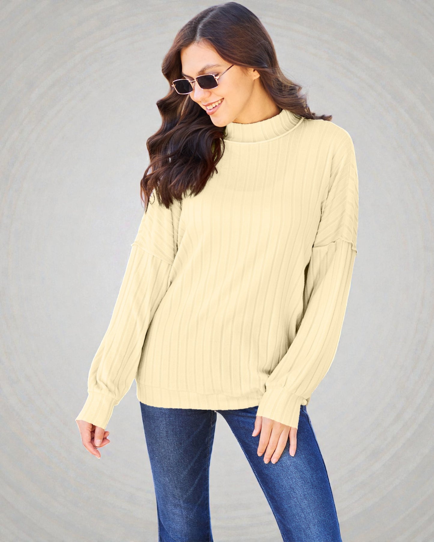 Woman wearing a beige sweater and blue jeans against a gray background