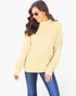 A woman wearing a pale yellow ribbed knit mock neck sweater and blue jeans, posing against a solid white background.