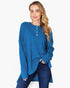 A woman modeling a blue ribbed knit long-sleeve top with a buttoned henley neckline, paired with dark blue jeans, against a plain white background.