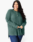 A woman modeling a green ribbed knit long-sleeve henley top with gold buttons, paired with blue jeans, against a plain white studio background.