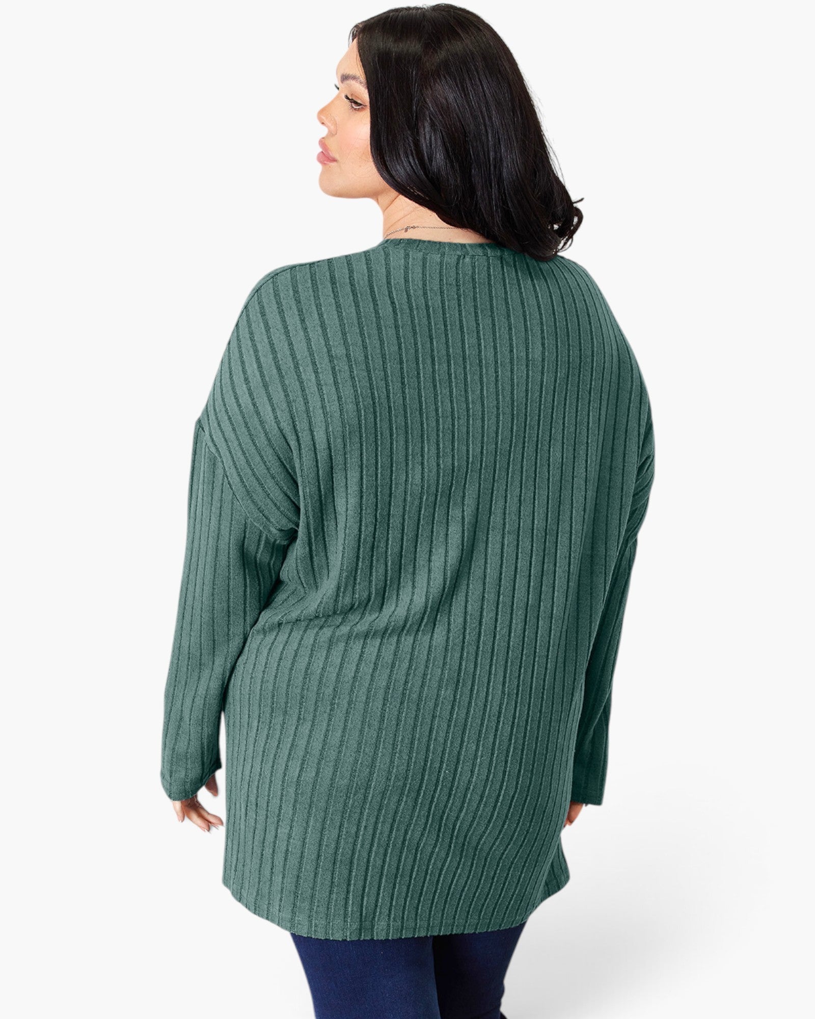 A woman shown from the back wearing a sage green ribbed knit sweater and dark blue jeans against a plain white studio background.