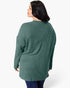 A woman shown from the back wearing a sage green ribbed knit sweater and dark blue jeans against a plain white studio background.
